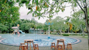 A circular water feature with seating around it, surrounded by trees and greenery. -  Villa CHR Syariah (Banjarbaru)