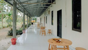 A covered corridor with a tiled floor, wooden tables and chairs, and a red basket. -  Villa CHR Syariah (Banjarbaru)