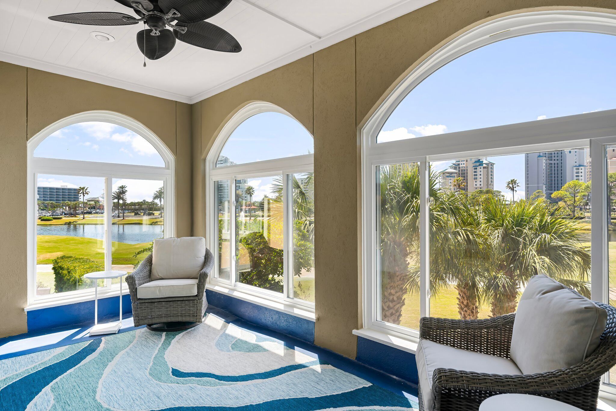 A sunroom with large arched windows, wicker furniture, and a view of a golf course and city buildings.