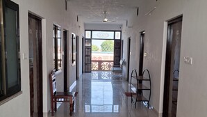 Un couloir avec un ventilateur de plafond, une vue sur l’extérieur et une chaise placée au centre.