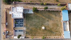 Vue aérienne d’un bâtiment avec un parking, une vaste zone herbeuse et une structure surmontée d’un toit bleu.