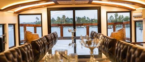 A dining area with leather booths, a glass table, and a view of the water outside.