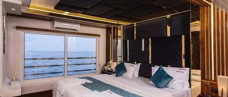 A modern bedroom with a large bed, a view of the sea, and a wooden ceiling.