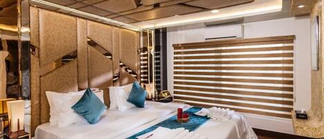 A hotel room with a large bed, a headboard with a geometric pattern, a bedside table with a lamp, and a window with blinds.