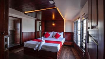A hotel room with a large bed, wooden paneling, a red accent wall, and a window with a view.