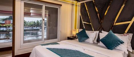 Habitación de hotel con una cama grande, vista a una masa de agua a través de una puerta corrediza y un diseño de cabecera moderno.