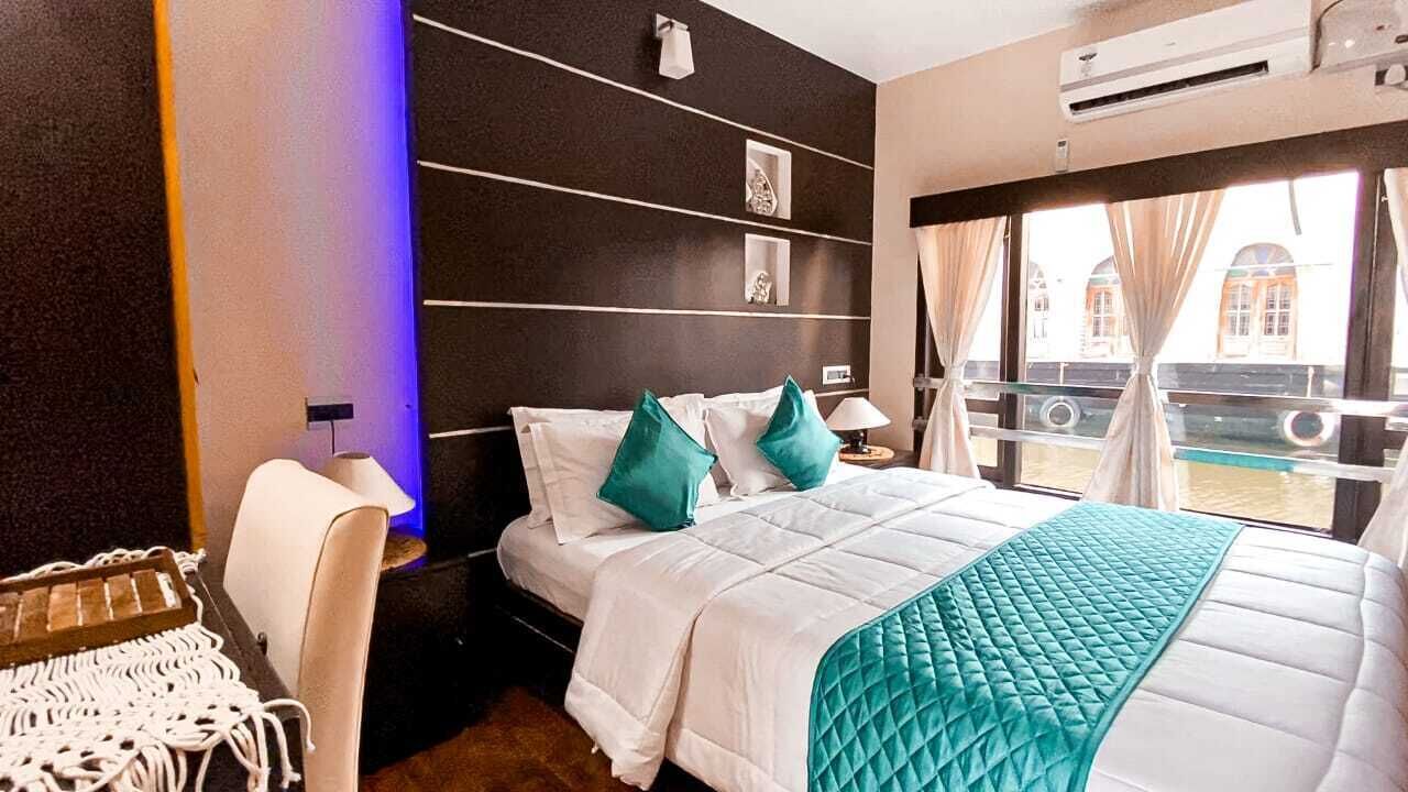 Ein Hotelzimmer mit Bett, Sessel, Nachttisch und Fenster mit Blick auf Gebäude.