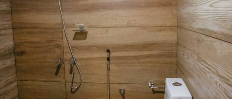 Un baño pequeño con paneles de madera, que incluye un inodoro, una ducha y un balde.