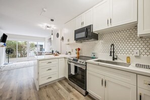 Een moderne keuken met witte kasten, een magnetron, een oven en een spoelbak.
