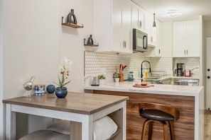 Een moderne keuken met witte kasten, een houten eiland en een barkruk.