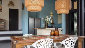 A dining area with a wooden table, white chairs, and woven pendant lights. - Blue Bay s Tropical Escape (Sint Michiel)