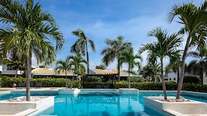 A swimming pool surrounded by palm trees and a building with a tiled roof. - Blue Bay s Tropical Escape (Sint Michiel)
