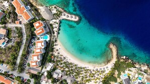 An aerial view of a coastal resort with multiple buildings, a sandy beach, and clear turquoise waters. - Blue Bay s Tropical Escape (Sint Michiel)