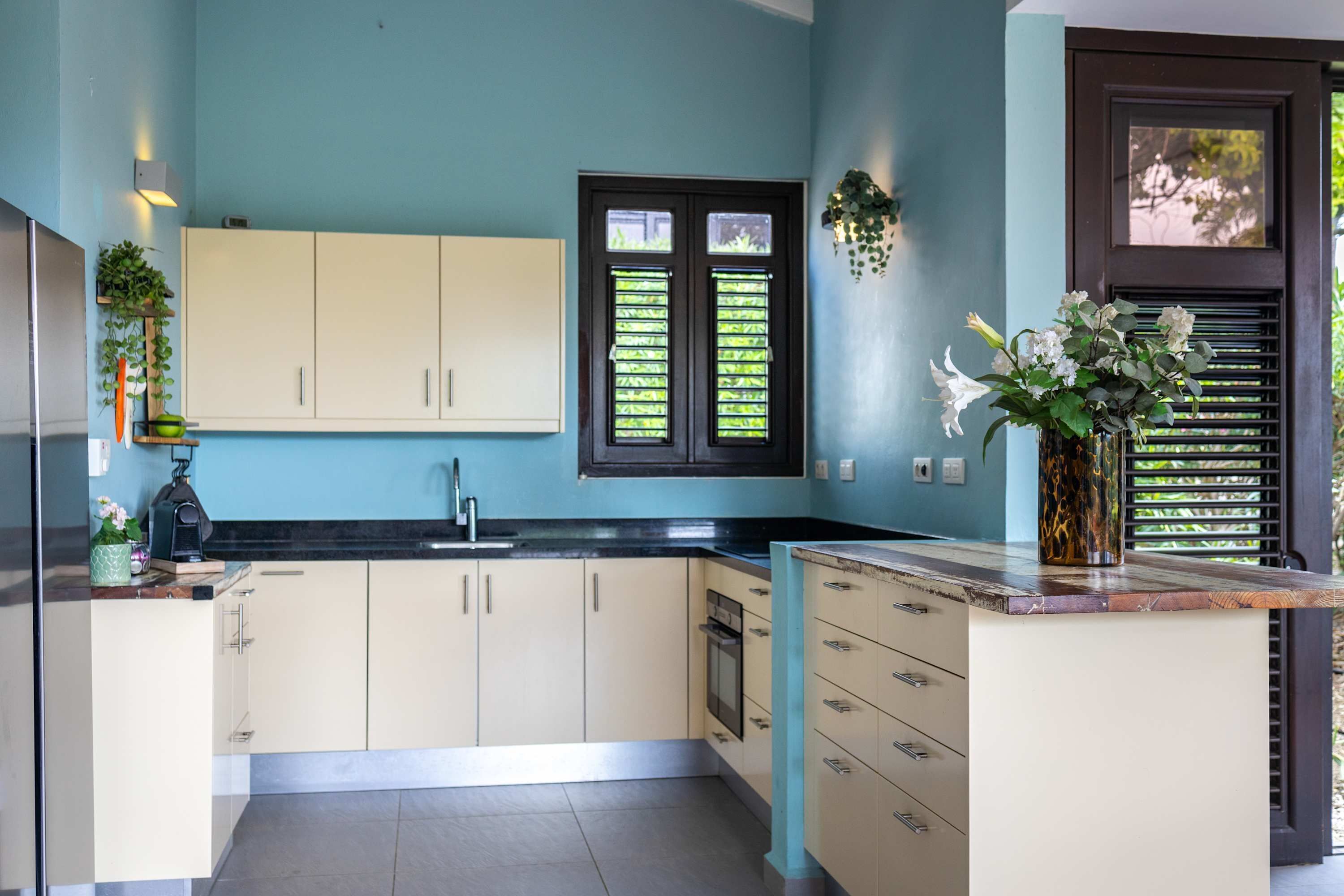 A modern kitchen with light-colored cabinets, a black countertop, and a window with shutters.