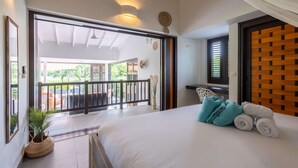 A bedroom with a large bed, a balcony with a view of the outside, and a wooden headboard. - Blue Bay s Tropical Escape (Sint Michiel)