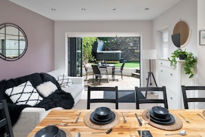 A modern kitchen with a dining area, featuring a stone wall, a grill, and a view of the garden.