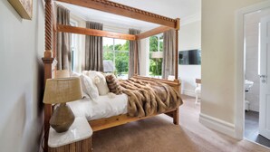 A four-poster bed with a fur throw, a lamp, and a view of the outdoors through large windows. - Rosemount X3 Bed Townehouse With Hot Tub (Windermere)