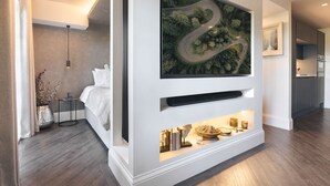 Et moderne hotelværelse med et stort, ophængt kunstværk, der viser en snoet vej gennem en skov, en indbygget hylde med dekorative genstande og en pænt redt seng.