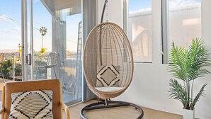 Ein modernes Zimmer mit einer großen Schiebeglasdoor, einem hängenden Korbstuhl, einem Holzstuhl mit gemustertem Kissen und einer Topfpflanze.