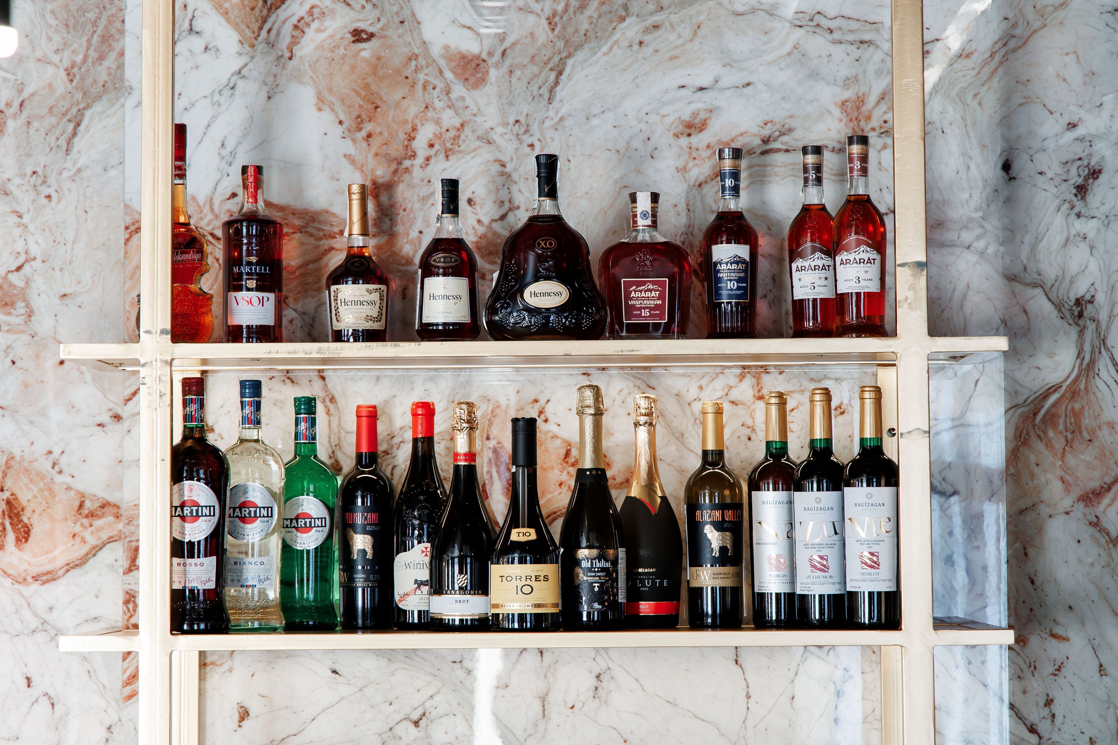 Two shelves of wine bottles against a marble background.