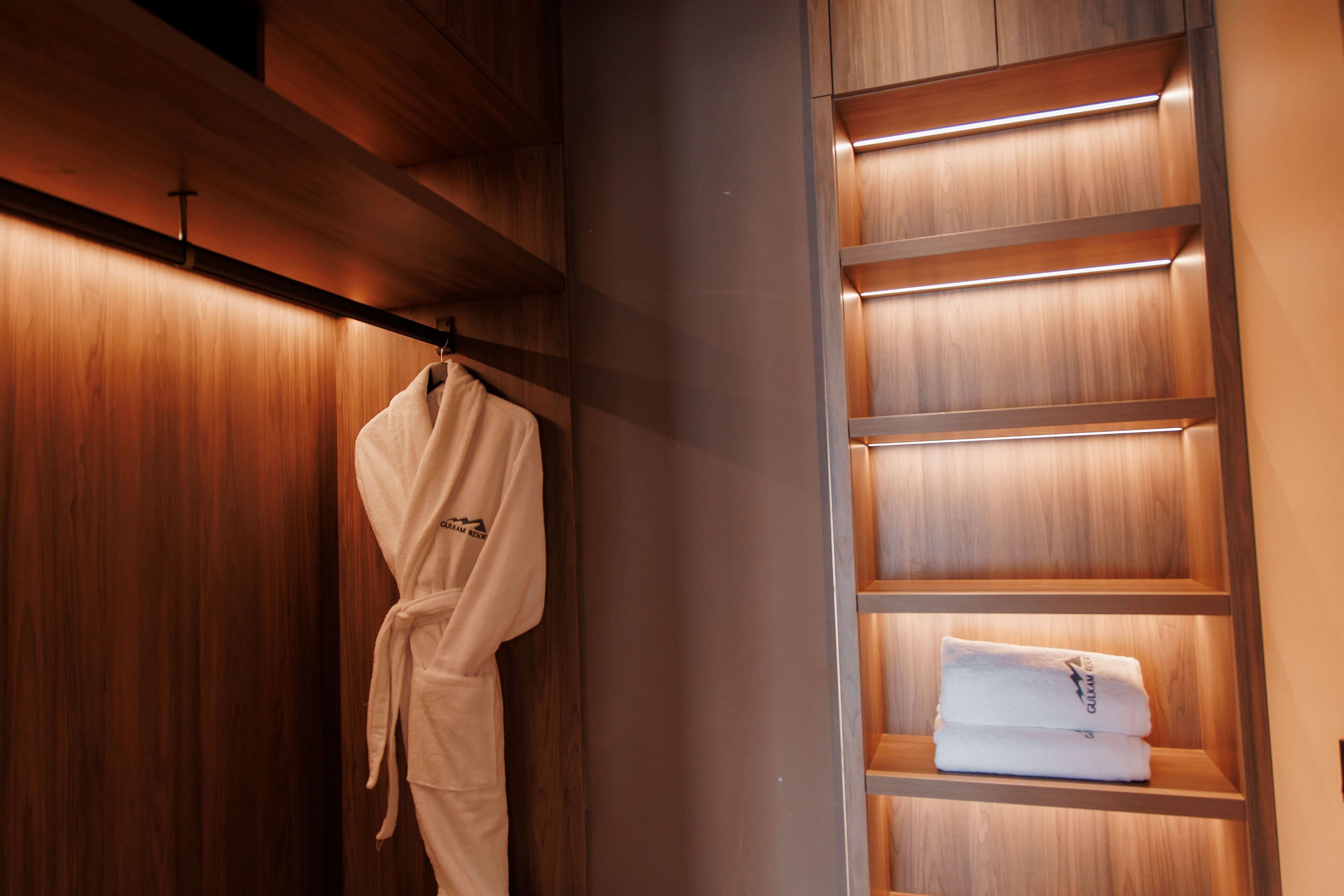A wooden wardrobe with a robe hanging on the door and a shelf with folded towels.