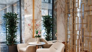 Un vestíbulo moderno con columnas de mármol, dos plantas en macetas, una mesa redonda con sillas y un biombo decorativo.