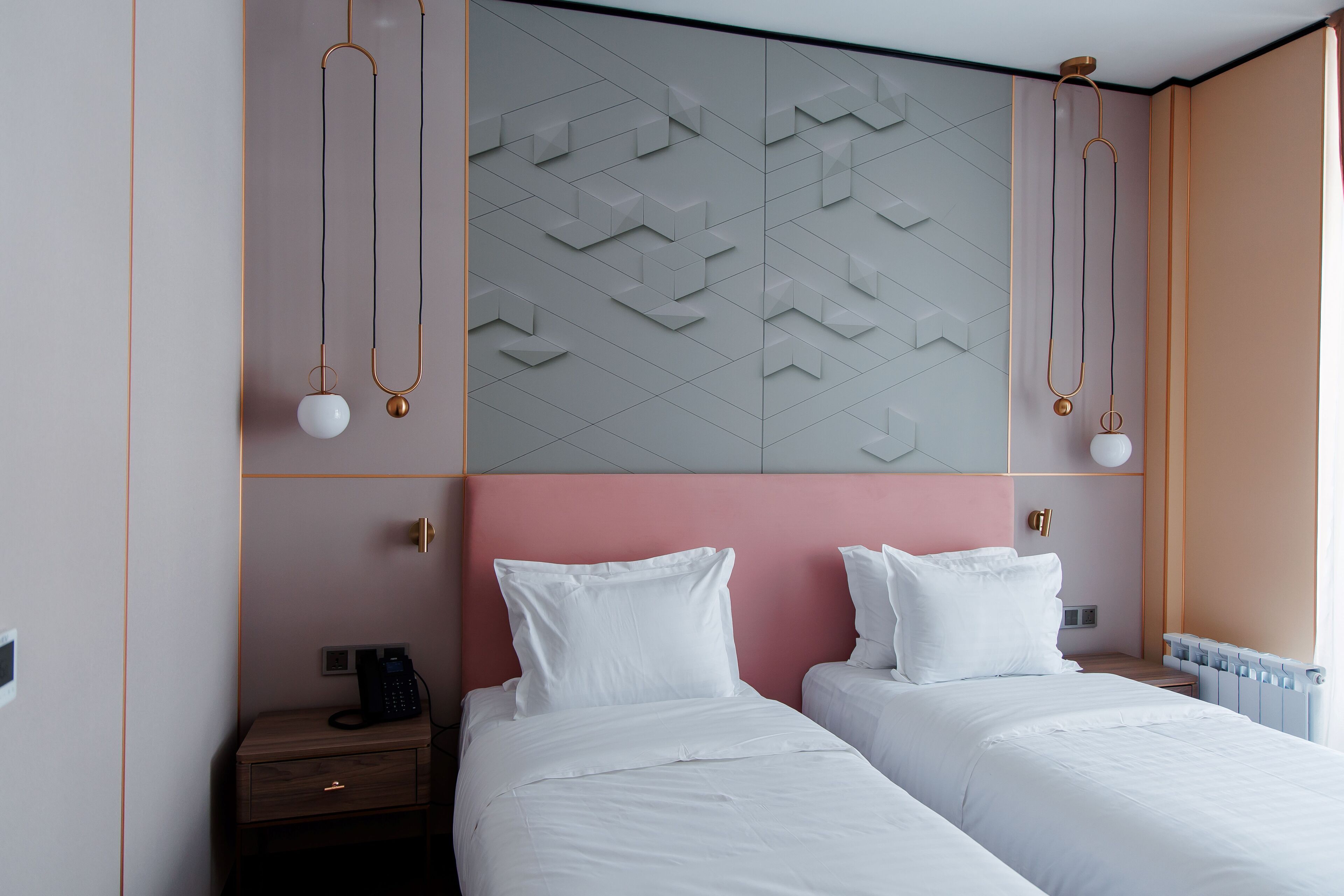 Ein Hotelzimmer mit zwei Betten, einem Nachttisch, einem an der Wand befestigten Telefon und einem Heizkörper.