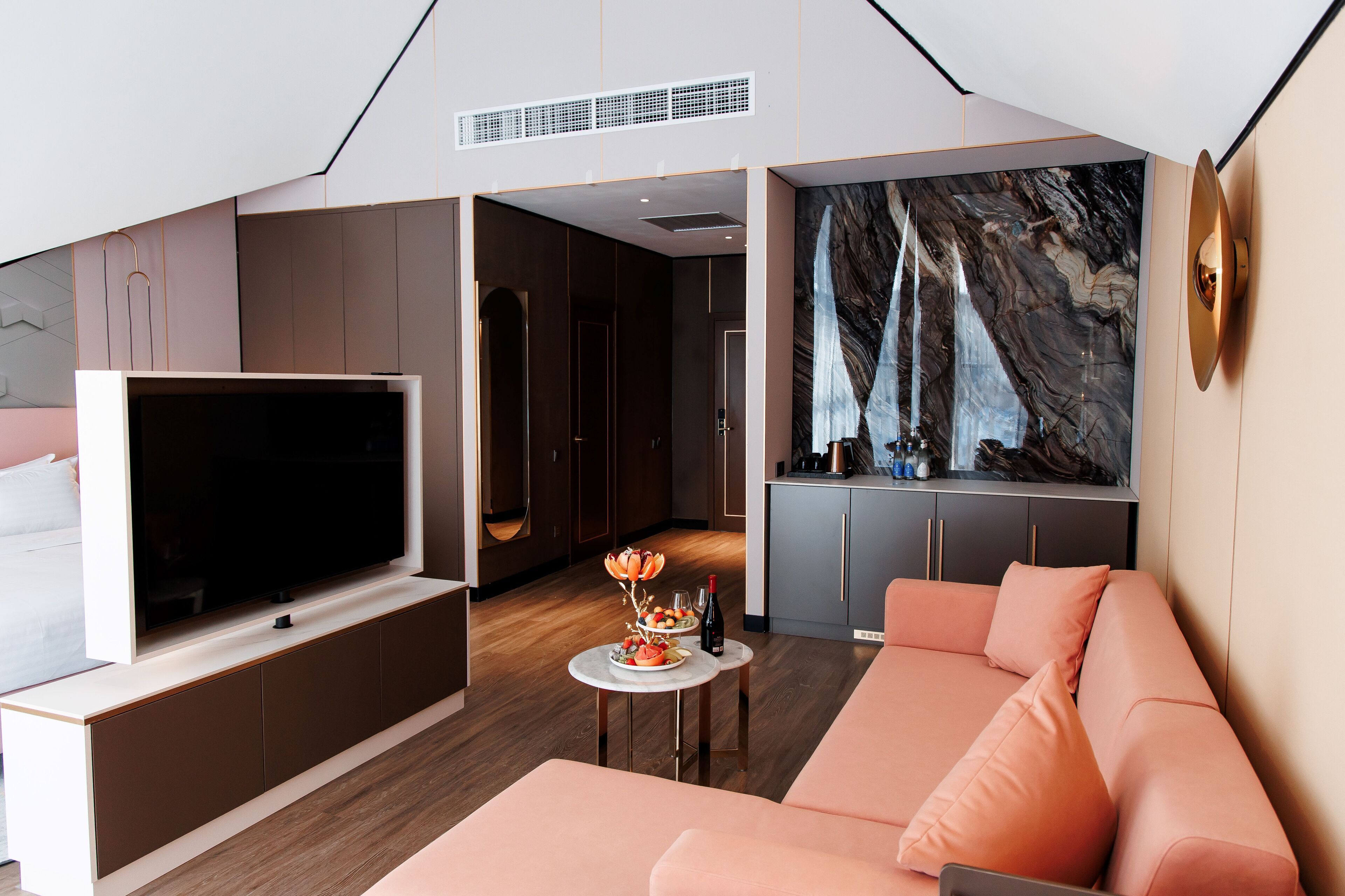 A modern living room with a flat-screen TV, a pink sofa, a marble wall, and a small round table with a decorative item.