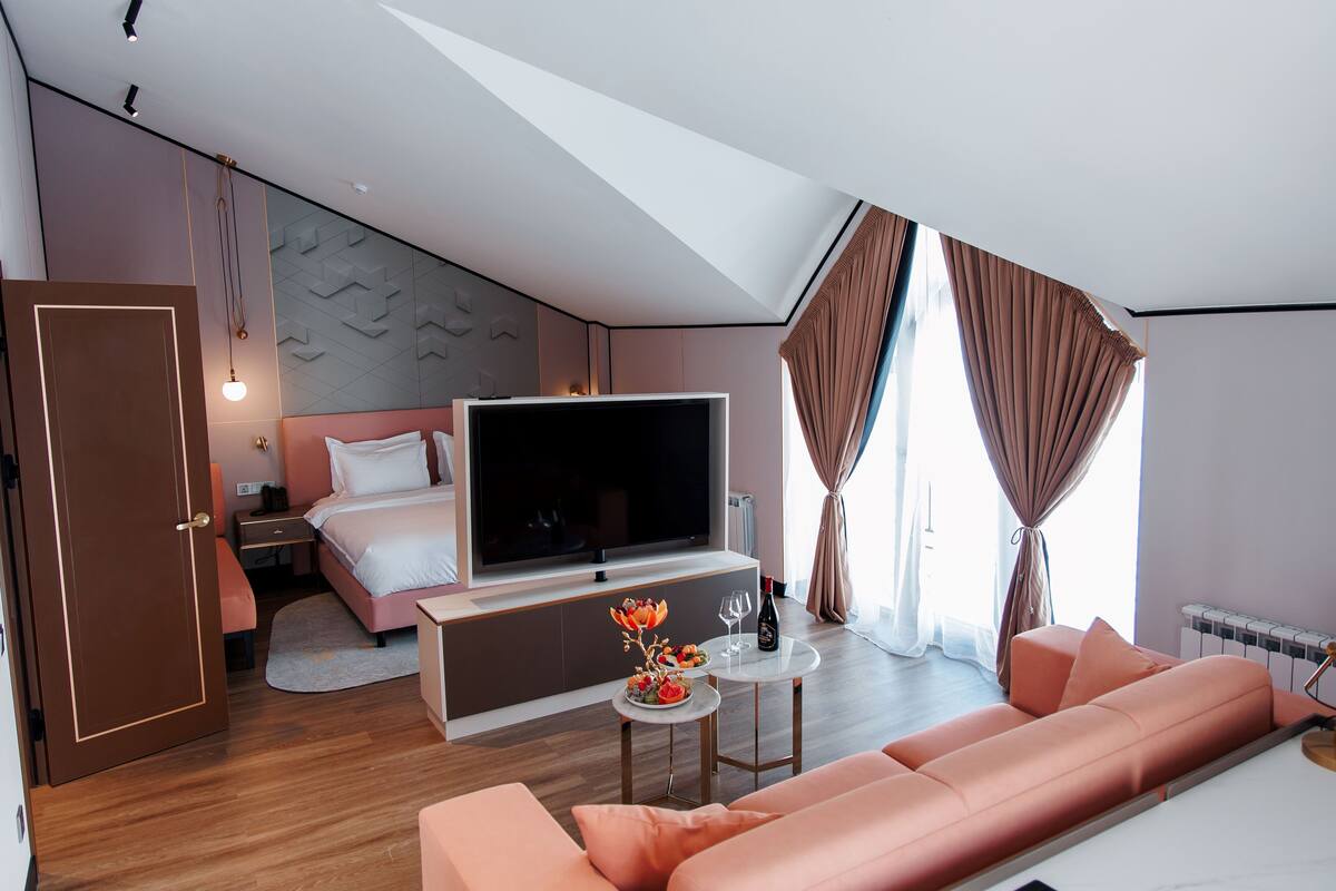 Quarto de hotel moderno com cama, TV, sofá e uma pequena mesa com um vaso de flores.
