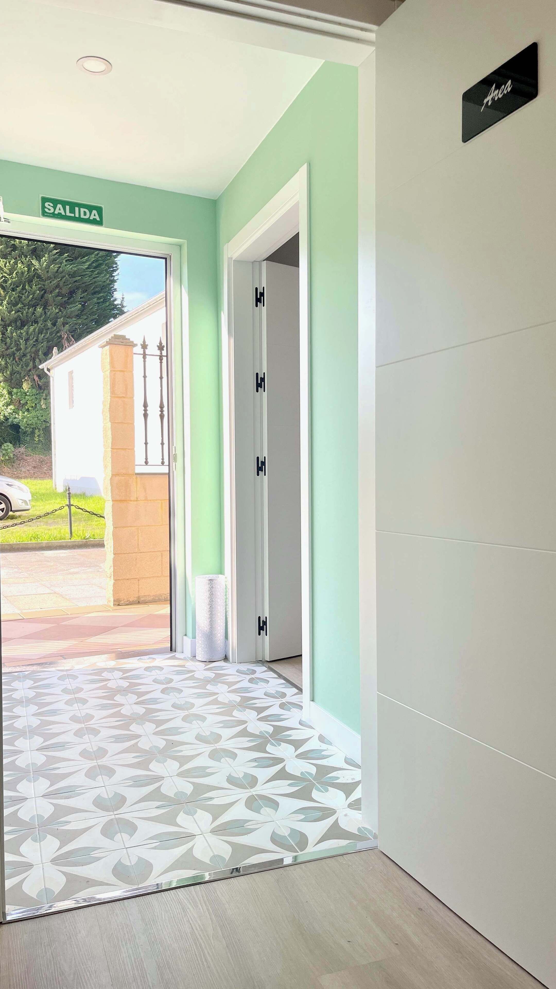 Un couloir avec un sol à motifs, une porte ornée d’un panneau noir en forme de « H », et un panneau « SALIDA » placé au-dessus.