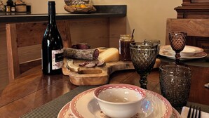 Une table de salle à manger en bois, avec une bouteille de vin, un panier de fruits et une planche à fromages.