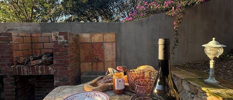 A table set outdoors with a bottle, glasses, and a basket of bread.