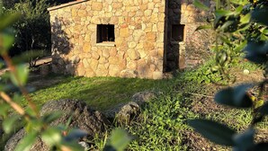 Un bâtiment en pierre avec deux fenêtres et une petite porte, entouré de verdure et sous un ciel dégagé.