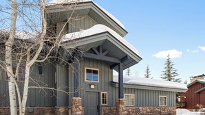 A two-story house with a stone foundation, a dark gray exterior, and a snow-covered roof.