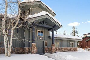 Una casa de dos pisos con cimientos de piedra, fachada gris oscuro y techo cubierto de nieve.