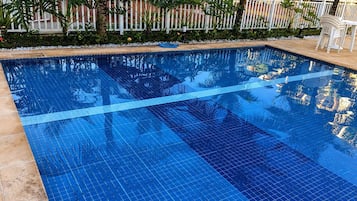 Une piscine d’un bleu éclatant, bordée de carreaux, avec une clôture blanche en arrière-plan.