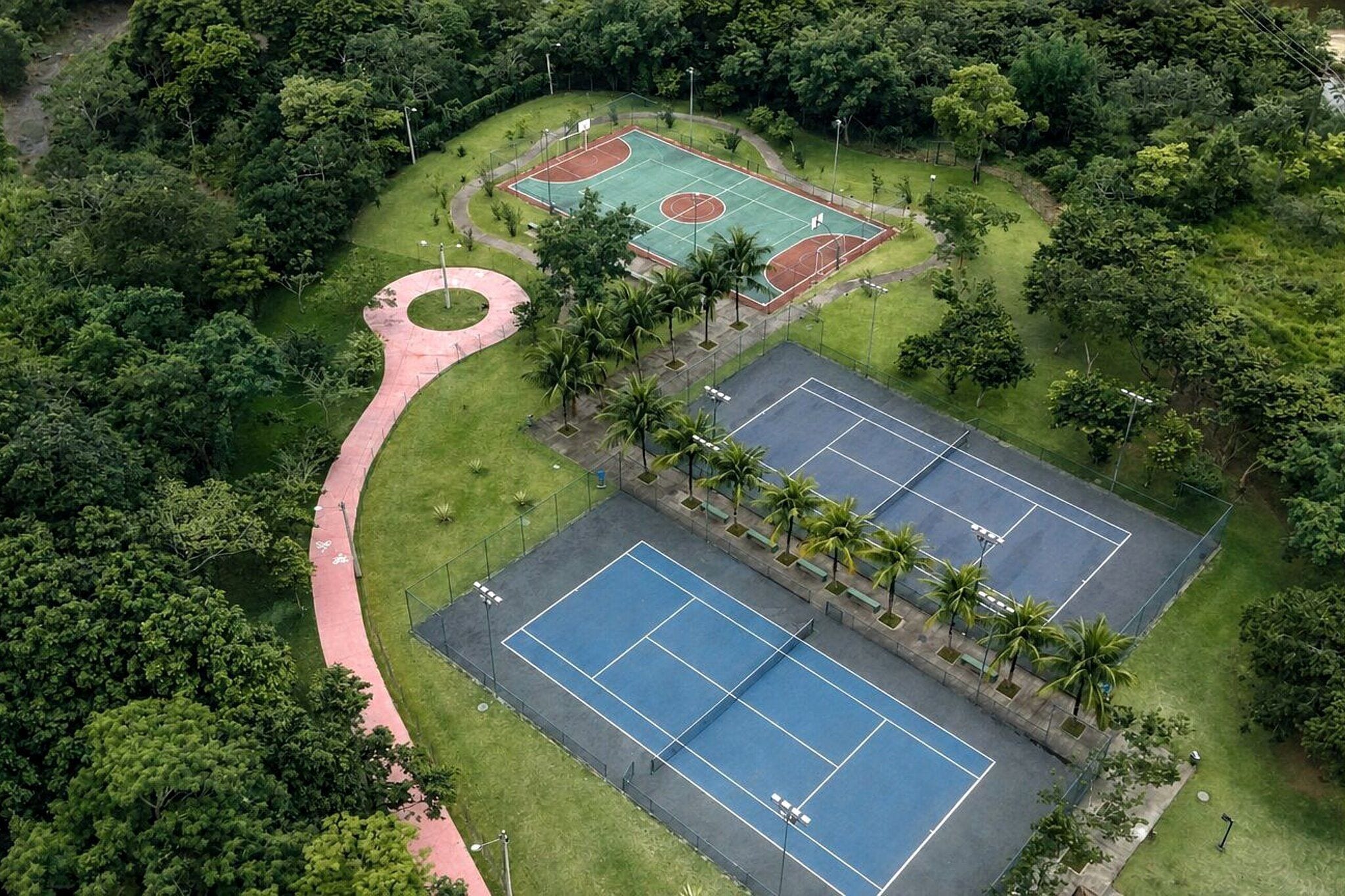 An aerial view of a sports complex with multiple tennis courts, a jogging track, and surrounding greenery.