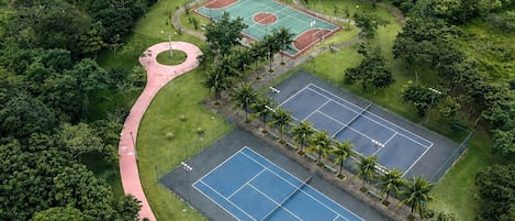 An aerial view of a sports complex with multiple tennis courts, a jogging track, and surrounding greenery.