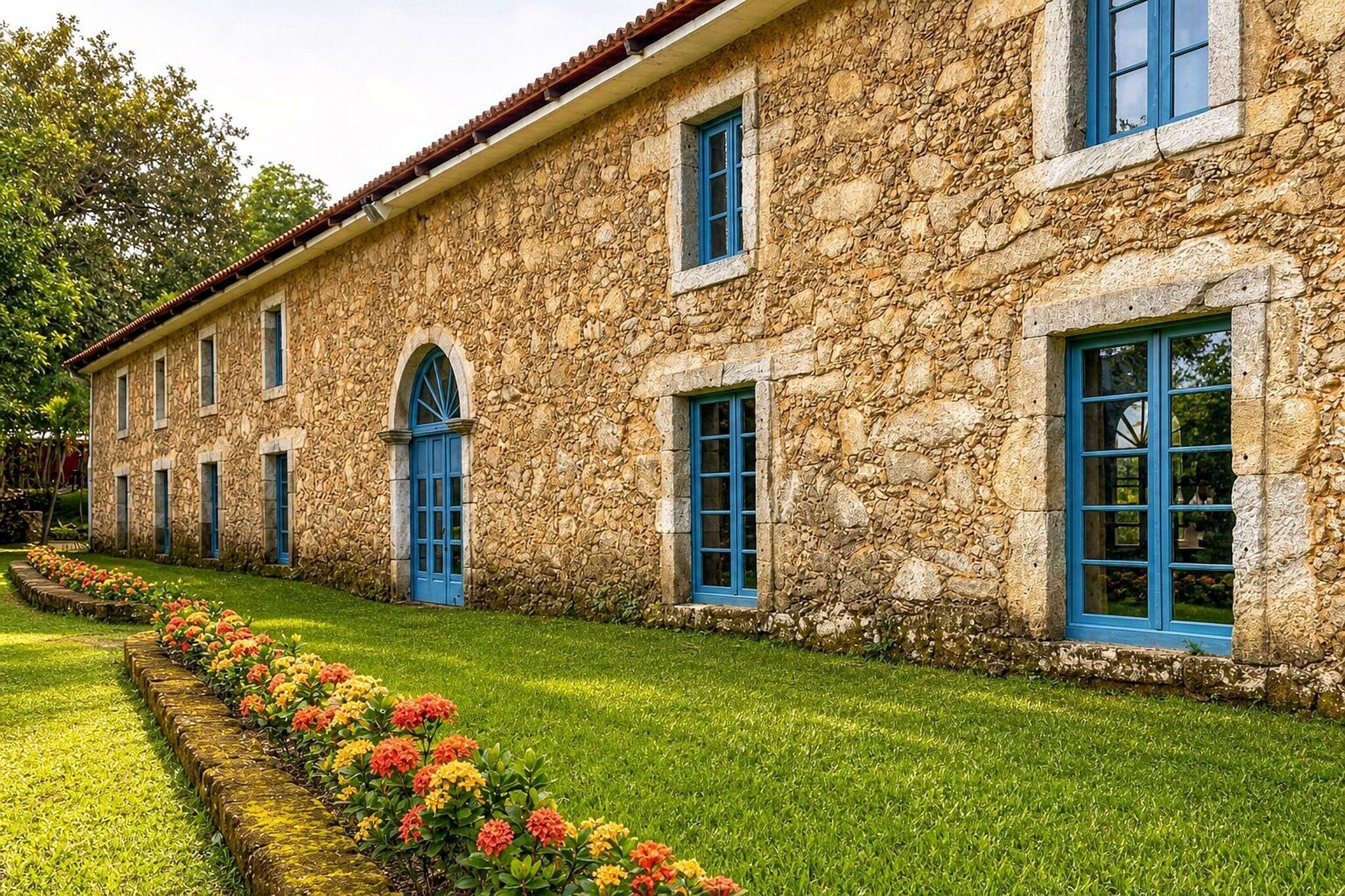 A stone building with multiple windows and a well-maintained lawn with colorful flowers.