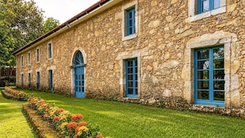 Un bâtiment en pierre doté de nombreuses fenêtres et d’une pelouse bien entretenue, agrémentée de fleurs aux couleurs vives.