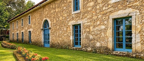 A stone building with multiple windows and a well-maintained lawn with colorful flowers.