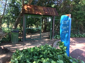 A shelter with a metal roof, a directional sign, and a green trash bin. - Reserva do Sahy, Condado (Mangaratiba)