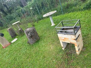 A barbecue grill outdoors with a metal frame and brick base, surrounded by grass and trees. - Reserva do Sahy, Condado (Mangaratiba)
