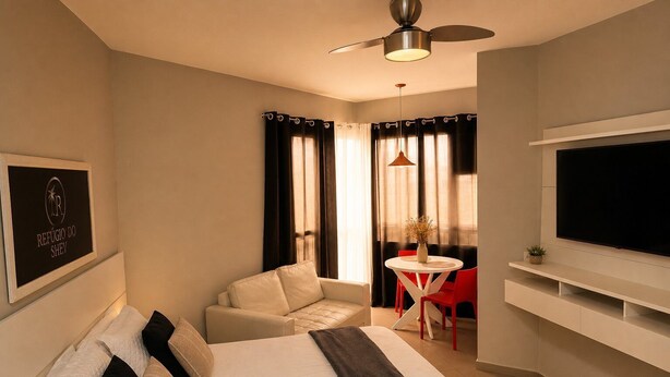 Ein Hotelzimmer mit einem Bett, einem Fernseher, einem Deckenventilator, einem kleinen Tisch mit Stühlen und einem Fenster mit Vorhängen.
