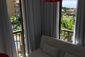 A balcony with a white sofa, curtains, and a view of a residential area. - Reserva do Sahy, Condado (Mangaratiba)