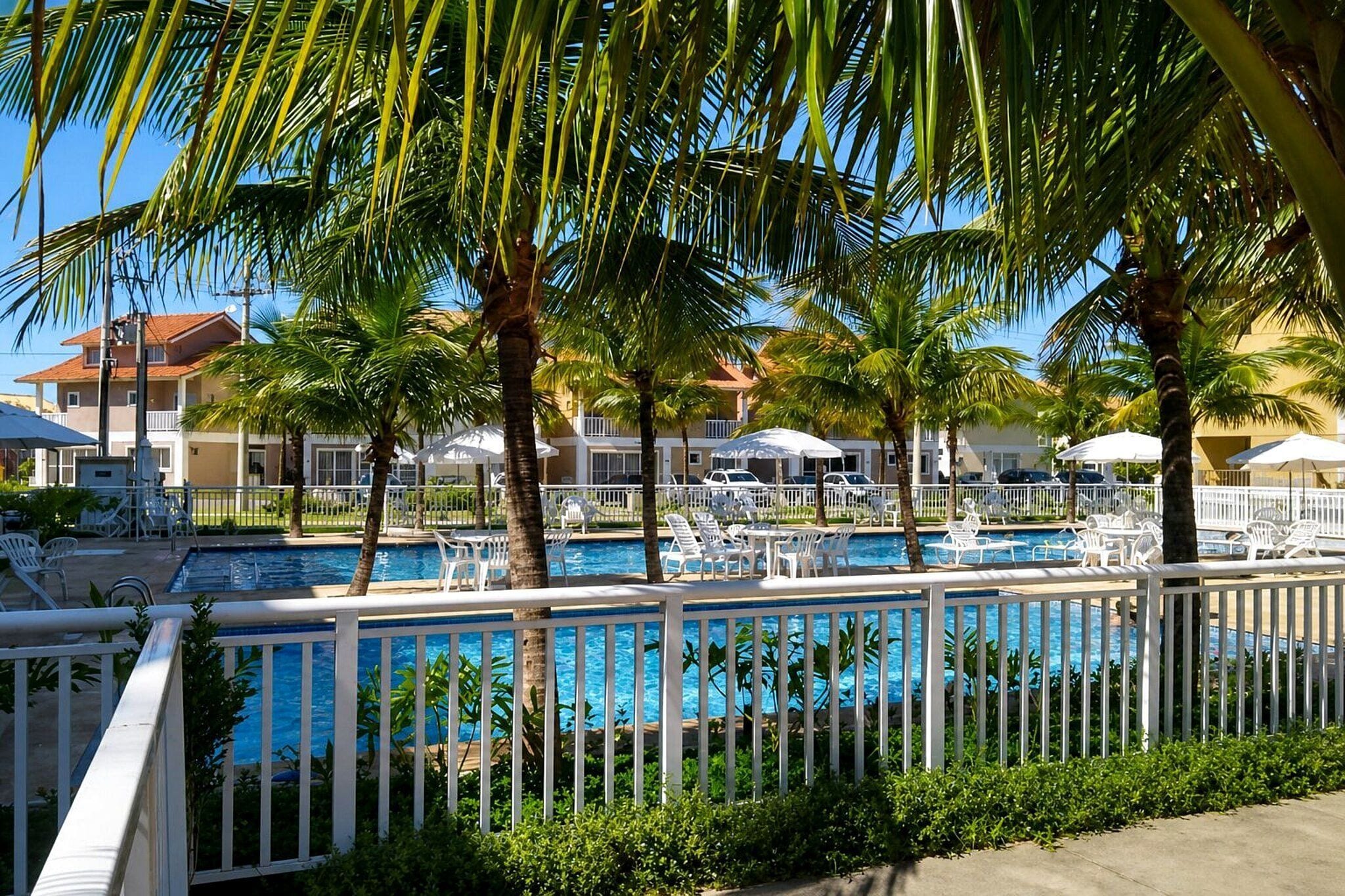 A pool area with multiple pools, surrounded by palm trees and white fences.