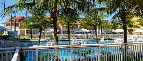 A pool area with multiple pools, surrounded by palm trees and white fences.