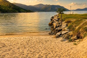 A sandy beach with a rocky shoreline, a small tree, and mountains in the background. - Reserva do Sahy, Condado (Mangaratiba)