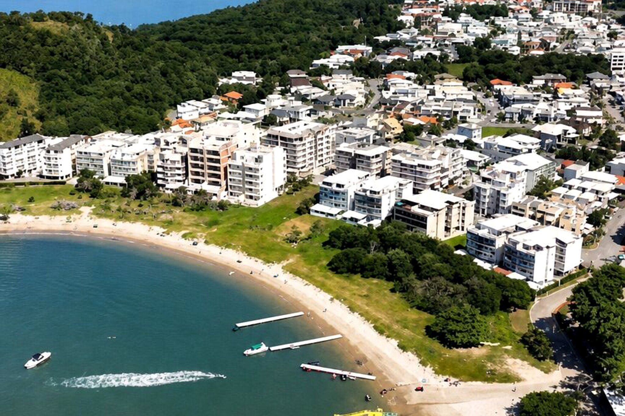 Un quartier résidentiel situé sur la côte, avec des immeubles à plusieurs étages, une plage de sable et une marina où sont amarrés plusieurs bateaux.