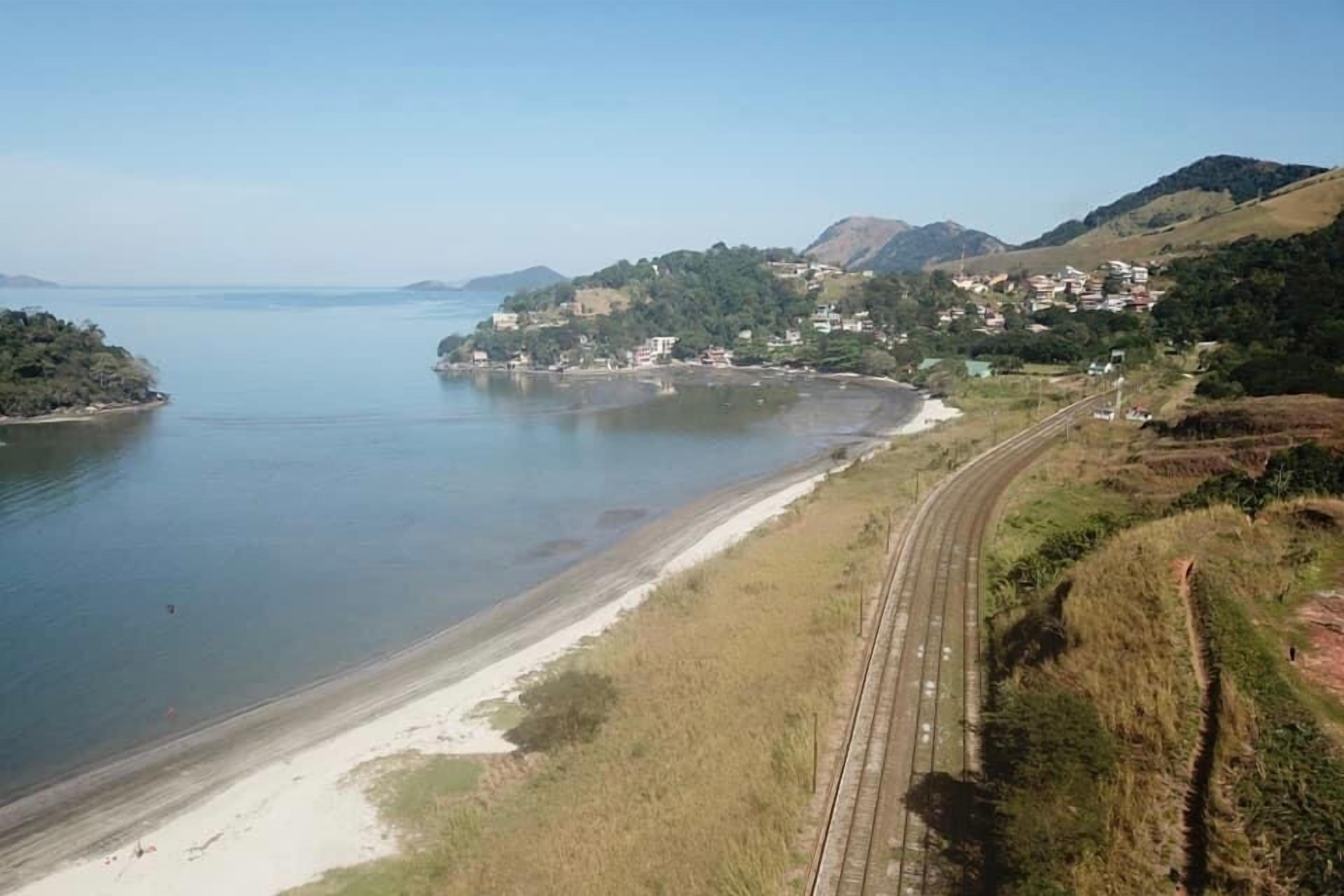 Uma área costeira com praia, trilhos de trem e um povoado numa encosta.